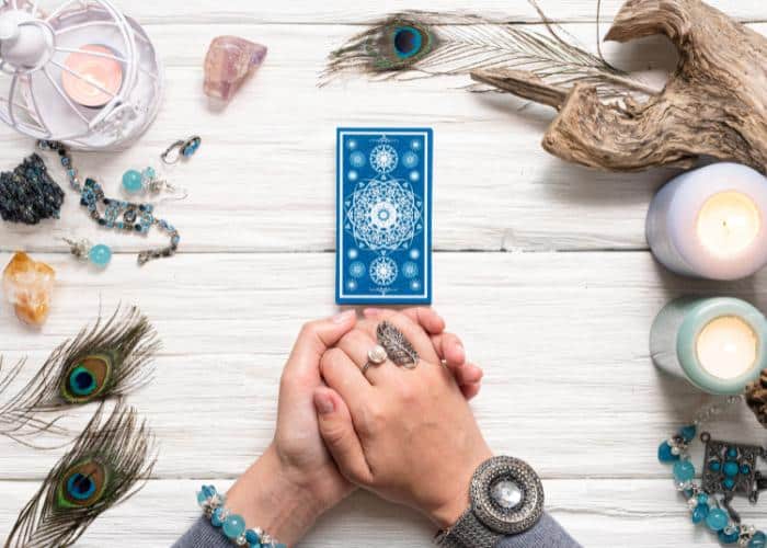 Overhead image of tarot cards and hands on a wood table with candles and objects around